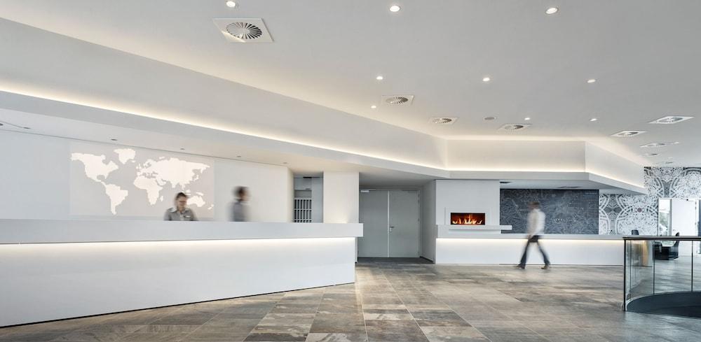 Mainport Hotel Rotterdam, A Hilton Affiliate Hotel Экстерьер фото The photo depicts a modern reception area. It features a sleek, brightly lit interior with white walls and smooth surfaces. There is a large reception desk at the front, where two people are seen working. Behind the desk, there is a large world map d