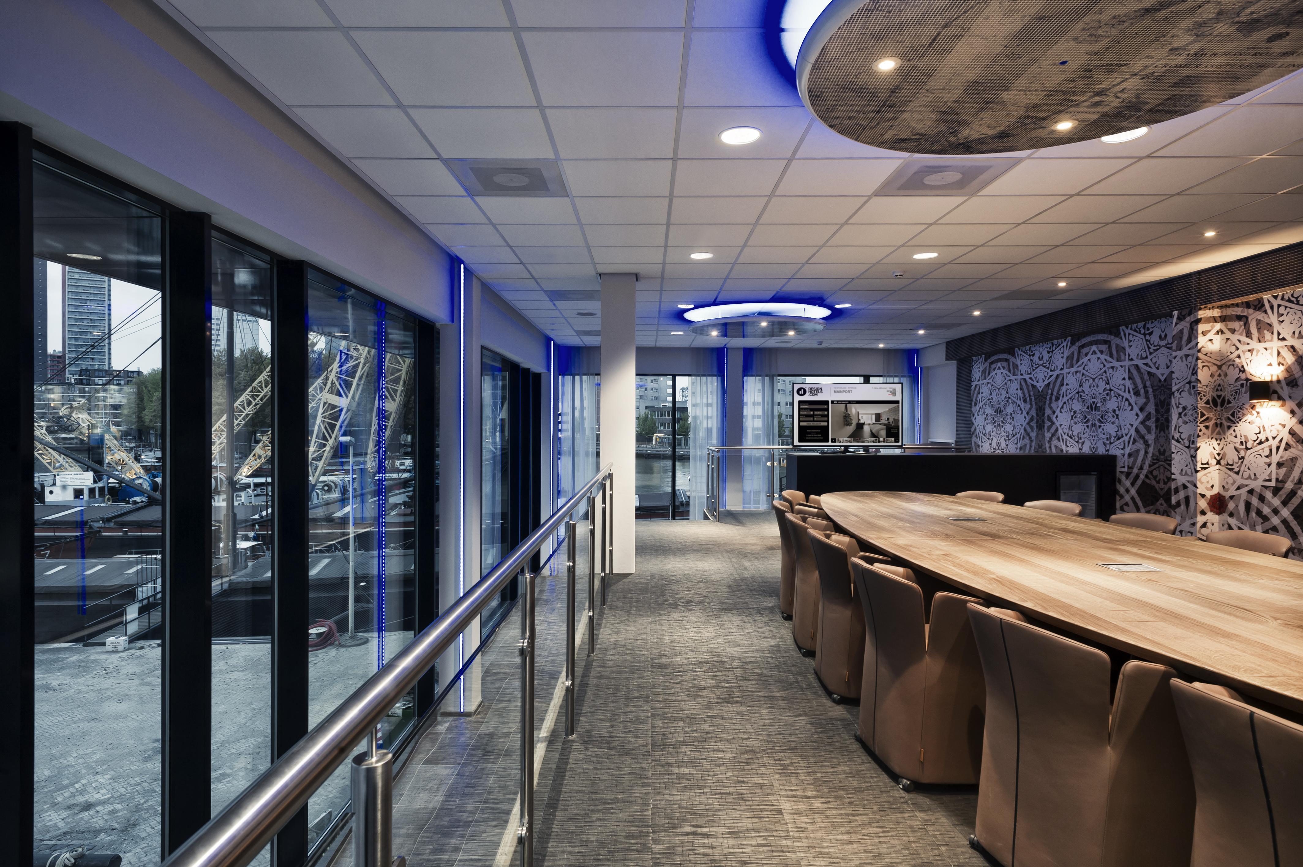 Mainport Hotel Rotterdam, A Hilton Affiliate Hotel Экстерьер фото The photo shows a modern interior space that appears to be a conference room or a meeting area. It features a long wooden table surrounded by brown upholstered chairs. The room has large glass windows that provide a view of the outside, possibly over