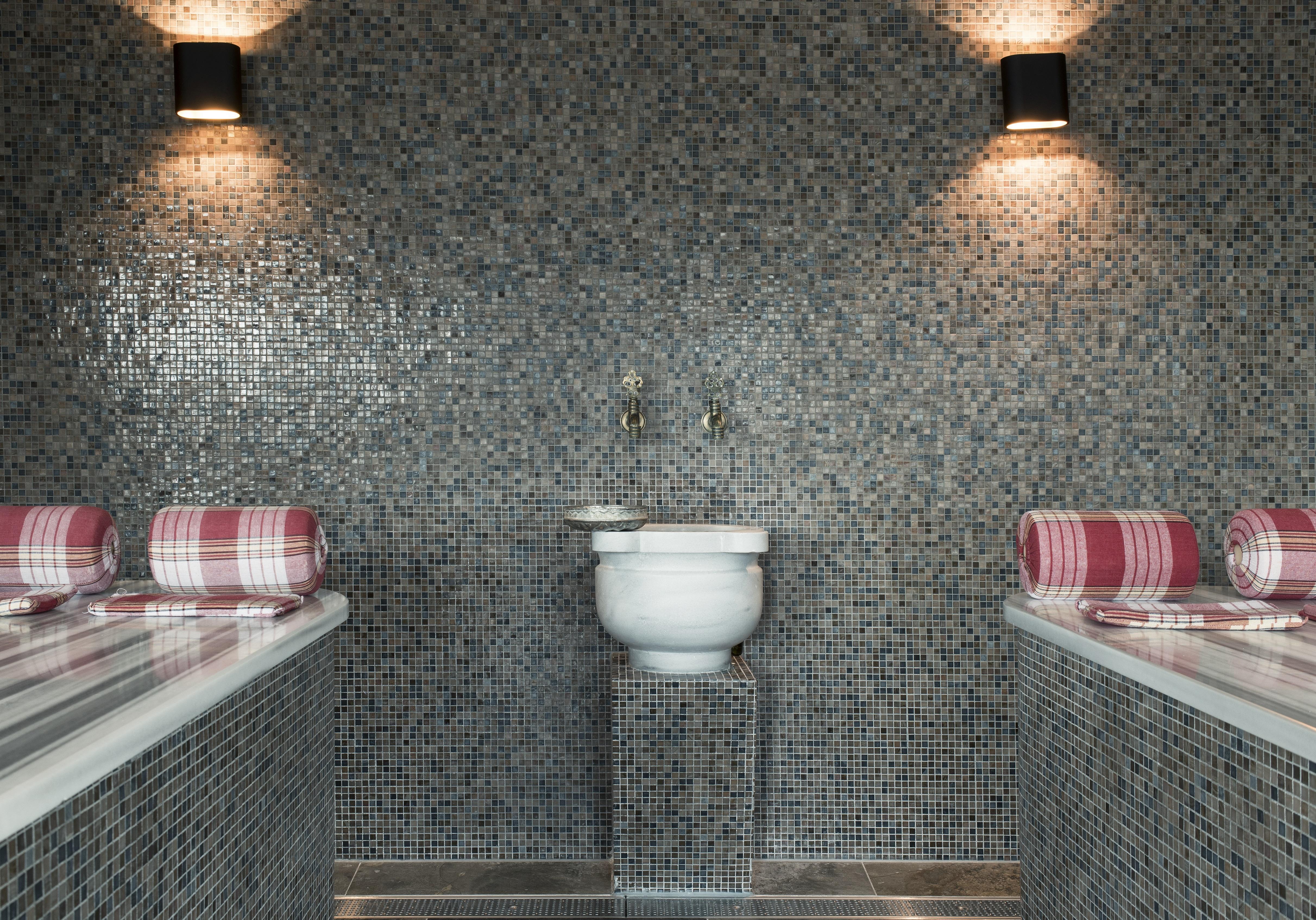Mainport Hotel Rotterdam, A Hilton Affiliate Hotel Экстерьер фото The photo shows a modern restroom or spa area with a sleek design. The walls are covered in small, grey mosaic tiles, creating a stylish and contemporary look. There are two bathing areas on either side, each with rolled towels placed on the ledge. I