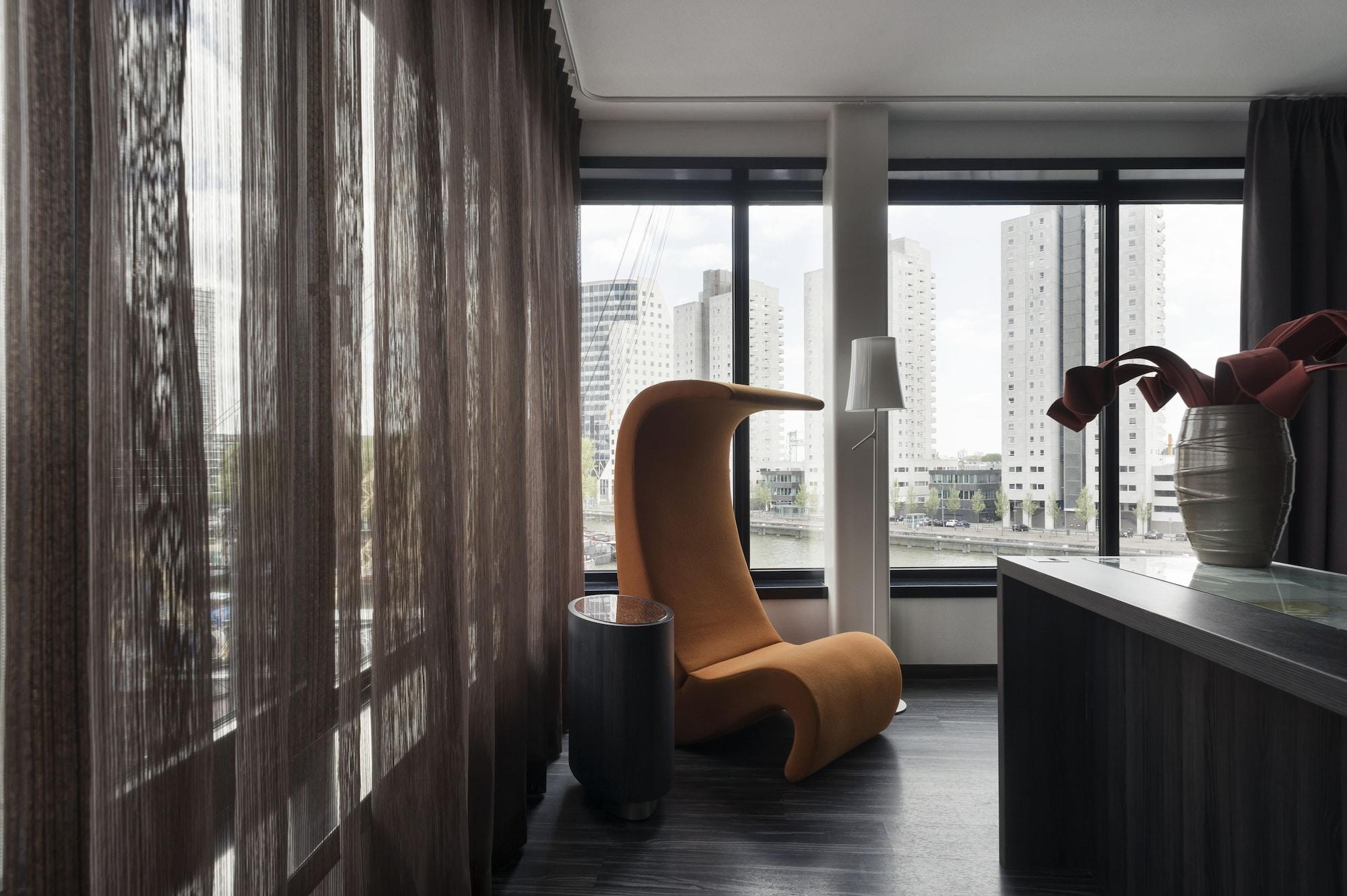 Mainport Hotel Rotterdam, A Hilton Affiliate Hotel Экстерьер фото The photo shows a modern interior space characterized by a stylish design. In the foreground, there is an eye-catching orange chair with a unique, curved shape. Next to it, there is a small, dark side table. The room features large windows with sheer